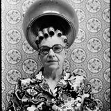 Eine alte Frau mit Brille sitzt unter einer Trockenhaube