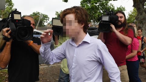Ein junger Mann mit rotbraunem Seitenscheitel und im Karohemd geht an mehreren Kameraleuten vorbei