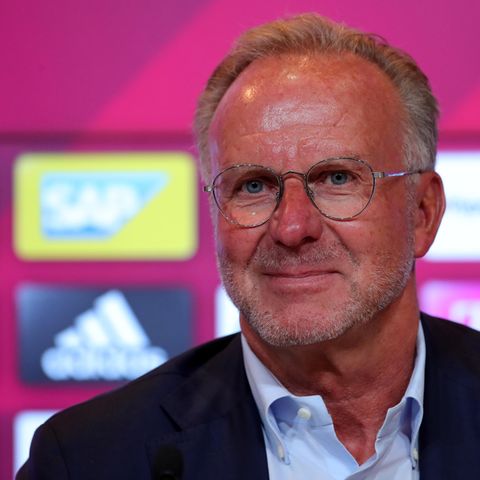 Karl-Heinz-Rummenigge, Vorstandsboss des FC Bayern München, sitzt in Hemd und Jackett vor einer Wand mit Sponsoren-Logos