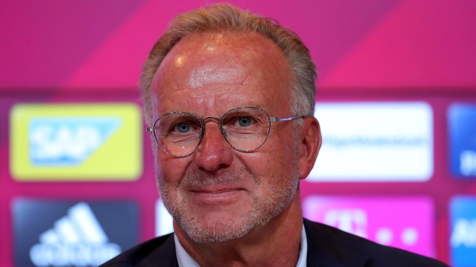 Karl-Heinz-Rummenigge, Vorstandsboss des FC Bayern München, sitzt in Hemd und Jackett vor einer Wand mit Sponsoren-Logos