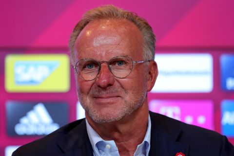 Karl-Heinz-Rummenigge, Vorstandsboss des FC Bayern München, sitzt in Hemd und Jackett vor einer Wand mit Sponsoren-Logos