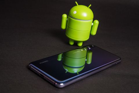 Das Android-Männchen steht neben einem Smartphone.
