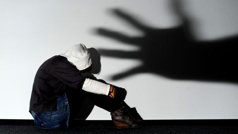 Ein Mädchen sitzt vor einer Wand, auf der der Schatten einer Hand groß zu sehen ist