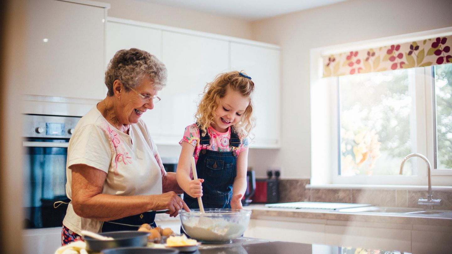Ein Mädchen mit blonden Locken und ihre Großmutter machen einen Kuchenteig