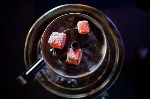 Glühende Kohle liegt auf einem Metallsieb über dem Tabak im Kopf einer Wasserpfeife in einer Shisha-Bar