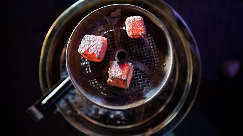 Glühende Kohle liegt auf einem Metallsieb über dem Tabak im Kopf einer Wasserpfeife in einer Shisha-Bar