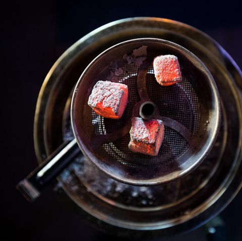 Glühende Kohle liegt auf einem Metallsieb über dem Tabak im Kopf einer Wasserpfeife in einer Shisha-Bar
