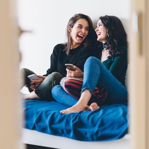Zwei junge Frauen sitzen lachend auf dem Bett