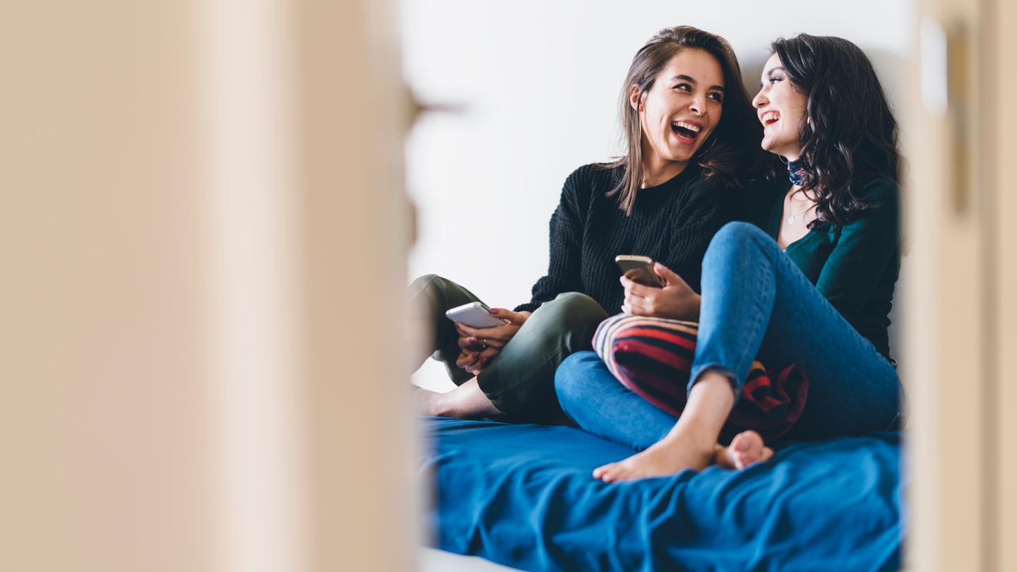 Zwei junge Frauen sitzen lachend auf dem Bett