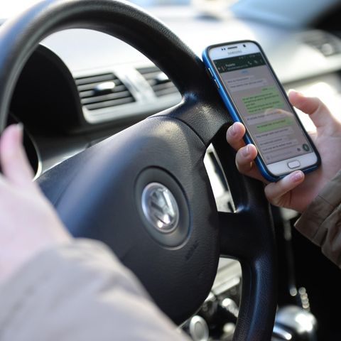 Eine Person hält während des Autofahrens ein Handy in der Hand