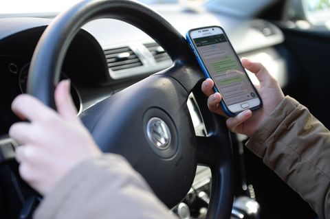 Eine Person hält während des Autofahrens ein Handy in der Hand