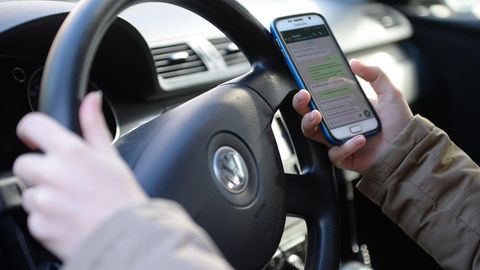 Eine Person hält während des Autofahrens ein Handy in der Hand