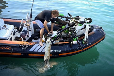 Ein Mann steht auf einem Boot und zieht einen E-Roller aus dem Wasser