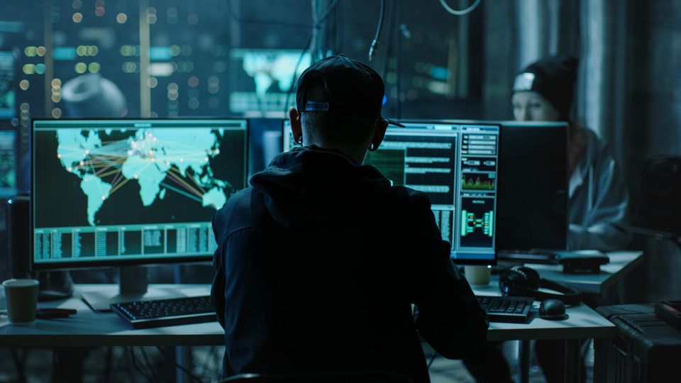 Junge Hacker sitzen in einem abgedunkelten Raum vor Bildschirmen