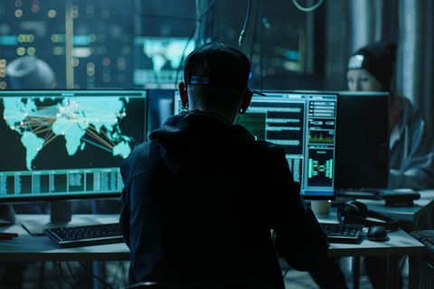 Junge Hacker sitzen in einem abgedunkelten Raum vor Bildschirmen