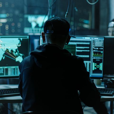 Junge Hacker sitzen in einem abgedunkelten Raum vor Bildschirmen