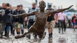 Ein Festivalbesucher springt in eine Schlammpfütze