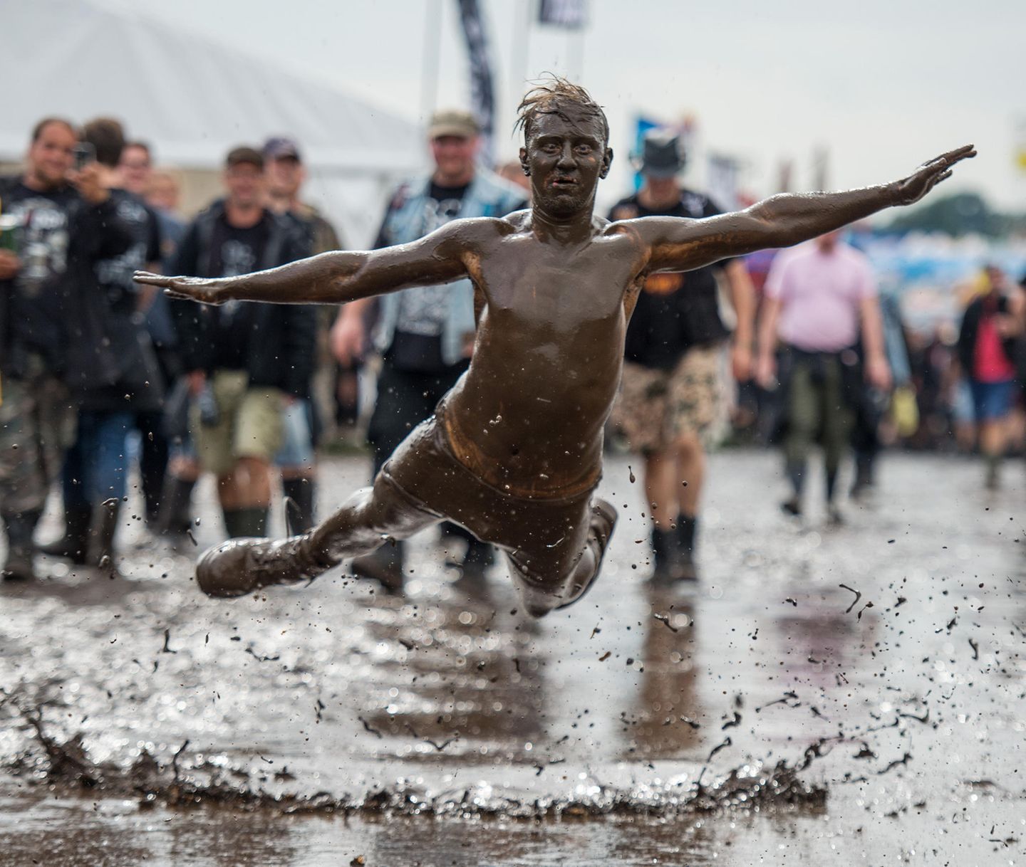 Ein Festivalbesucher springt in eine Schlammpfütze