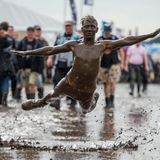 Ein Festivalbesucher springt in eine Schlammpfütze