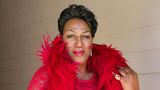 Eine große afrikanische Trans-Frau in einem knallroten Kleid und einer Boa