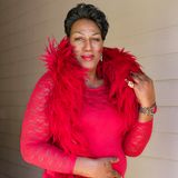 Eine große afrikanische Trans-Frau in einem knallroten Kleid und einer Boa