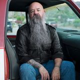 Sky sitzt mit langem grauen Bart und Lederjacke im Auto