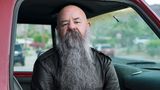 Sky sitzt mit langem grauen Bart und Lederjacke im Auto