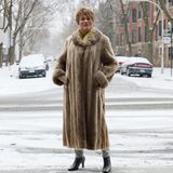 Eine farbige Frau steht im langen Pelzmantel auf einer schneebedeckten Straße