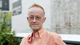 Ein älterer Mann mit Brille sitzt auf einer Gartenbank