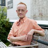 Ein älterer Mann mit Brille sitzt auf einer Gartenbank