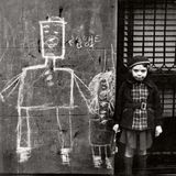 Ein Mädchen steht neben einer mit Kreide bemalten Hauswand