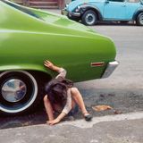 Ein Mädchen hockt zwischen einem parkenden Auto und dem Bürgersteig