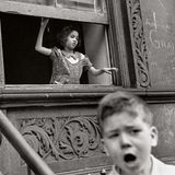Ein Mädchen unterhält sich aus dem Fenster ihrer Wohnung mit Kindern auf der Straße