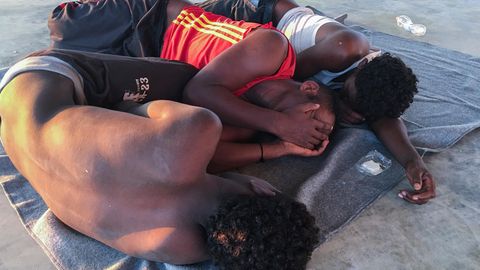 Die Aufnahme zeigt drei gerettete Bootsflüchtlinge, die verzweifelt in einem Migrantenlager in Libyen gestrandet sind.