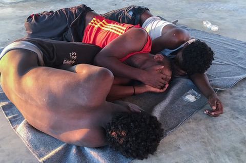 Die Aufnahme zeigt drei gerettete Bootsflüchtlinge, die verzweifelt in einem Migrantenlager in Libyen gestrandet sind.