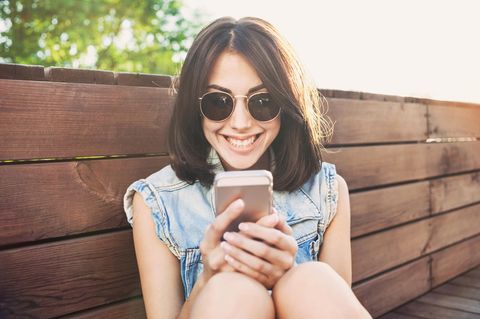 Eine junge Frau schaut grinsend auf ihr Handy