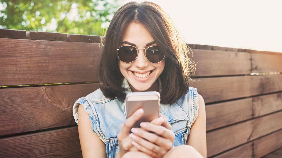 Eine junge Frau schaut grinsend auf ihr Handy
