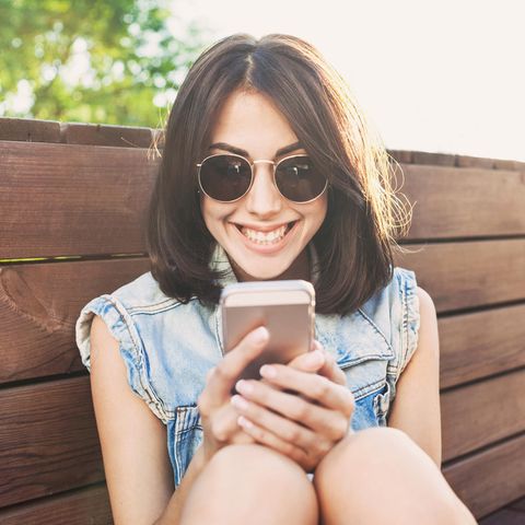 Eine junge Frau schaut grinsend auf ihr Handy