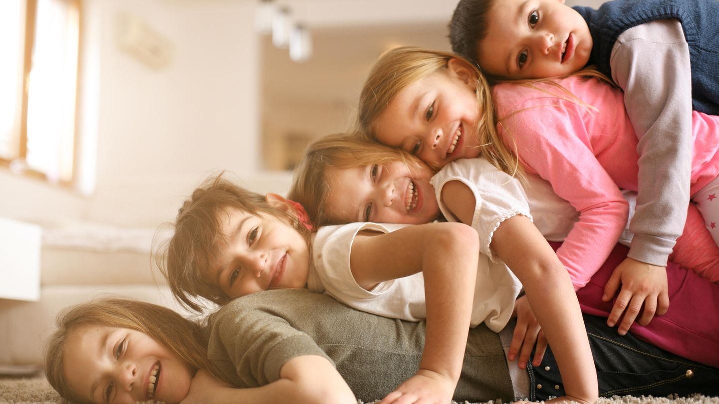 Kinder liegen übereinandergestapelt auf dem Teppich