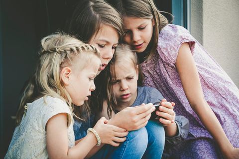 Schwestern unterschiedlichen Alters schauen gemeinsam auf ein Smartphone