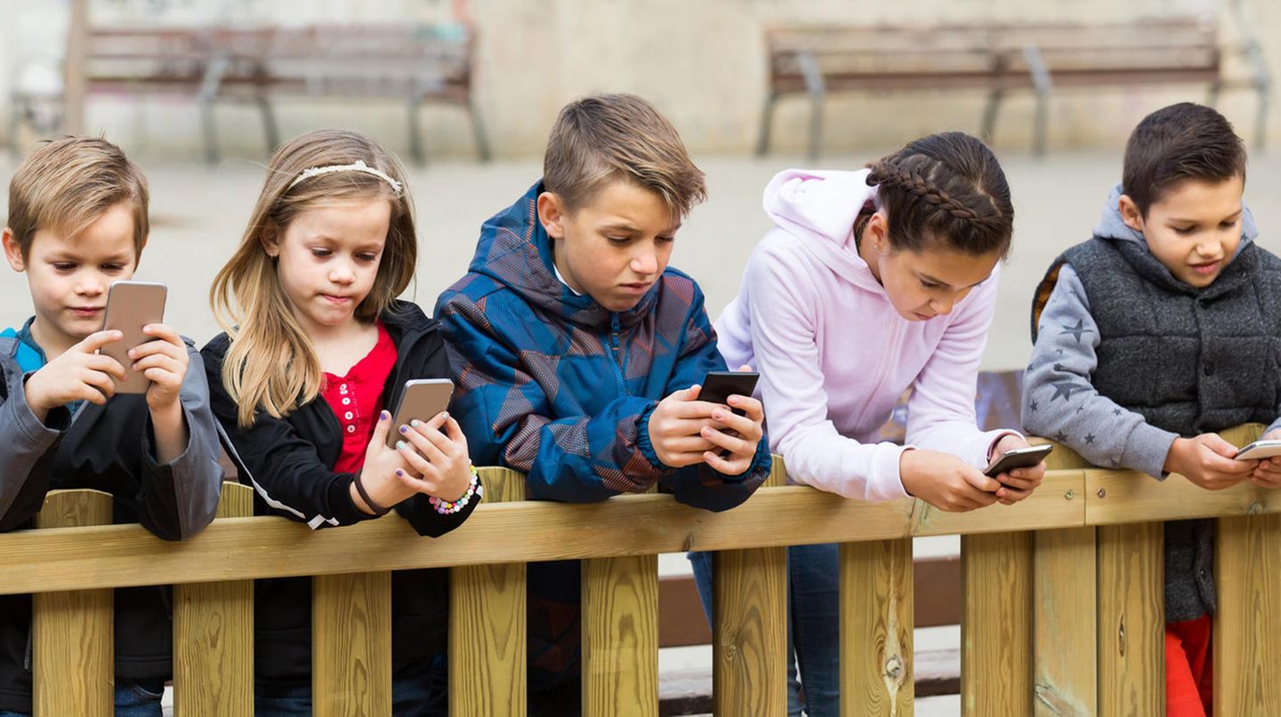 Mehrere Kinder lehnen an einen Gartenzaun und gucken auf ihr Smartphone