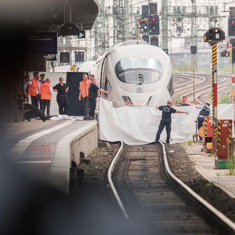 Polizisten und Feuerwehrleute spannen im Hauptbahnhof eine weiße Plane als Sichtschutz vor einen ICE