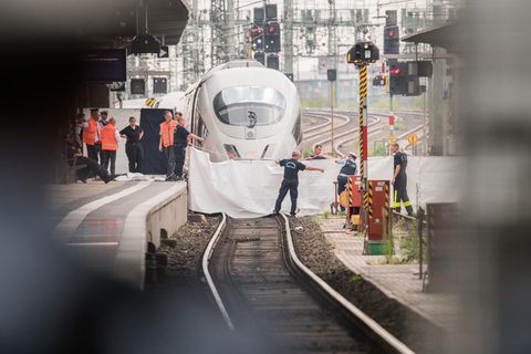 Polizisten und Feuerwehrleute spannen im Hauptbahnhof eine weiße Plane als Sichtschutz vor einen ICE