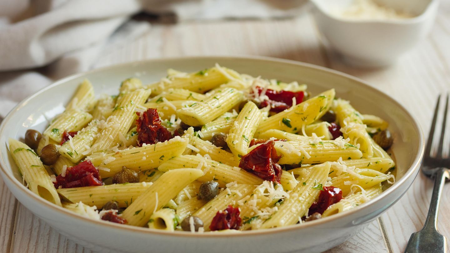 Nudelsalat mit getrockneten Tomaten  Zutaten:  Für die halb getrockneten Tomaten: 1 kg Cocktailtomaten, 1 EL Zucker, Meersalz, schwarzer Pfeffer aus der Mühle, 1 EL Thymianblättchen, 4 EL natives Olivenöl extra  Für den Salat: 500 g kurze Nudeln (z. B. Fusilli), Meersalz, 50 g Pinienkern, 2 Kugeln Büffelmozzarella (à 125 g Abtropfgewicht), 60 g Parmesan, 1 großes Bund Basilikum, 150 g Rucola  Für die Sauce: 6 EL Aceto balsamico, 4 EL Zitronensaft, 1 EL Akazienhonig, 100 ml Gemüsebrühe, Meersalz, schwarzer Pfeffer aus der Mühle, 8 EL natives Olivenöl extra  Zubereitung: Am Vorabend den Backofen auf 200 °C (Umluft 180 °C) vorheizen. Die Tomaten waschen, trocken reiben und halbieren. Ein Backblech mit Backpapier belegen und die Tomaten mit der Schnittfläche nach oben darauf verteilen. Zucker, 2 Teelöffel Meersalz, reichlich Pfeffer und die Thymianblättchen mischen und über die Tomaten streuen. Mit Olivenöl beträufeln. Das Backblech in den heißen Ofen schieben und die Tomaten 20 Minuten garen. Dann den Ofen ausschalten und die Tomaten über Nacht in der Resthitze des Backofens trocknen lassen.  Am nächsten Tag die Nudeln in reichlich Salzwasser bissfest kochen, dann durch ein Sieb abgießen, unter fließendem kaltem Wasser abschrecken und abtropfen lassen.  Pinienkerne in einer Pfanne ohne Fett goldbraun rösten, leicht salzen und beiseite stellen. Den Mozzarella abtropfen lassen und in kleine Stücke zupfen. Den Parmesan grob reiben oder in kleine Stücke brechen. Basilikum waschen und trocken schütteln. Die Blätter von den Stängeln zupfen und etwas kleiner zupfen. Den Rucola verlesen, waschen, trocken schleudern und in einen Gefrierbeutel füllen. Den Beutel verschließen und bis zum Servieren im Kühlschrank aufbewahren.  Für die Sauce Aceto balsamico, Zitronensaft, Honig, Gemüsebrühe, etwas Meersalz, reichlich Pfeffer und das Olivenöl kräftig verrühren. Nudeln, Tomaten, Mozzarella, Parmesan und Basilikum mit der Sauce in einer großen Schüssel mischen und mindestens 30 Minuten ziehen lassen.  Zum Servieren den Salat durchmischen und bei Bedarf nachwürzen. Dann den Rucola unterheben und den Salat anrichten. Mit den Pinienkernen bestreuen.
