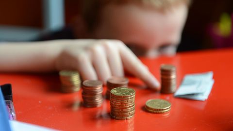 Ein Kind sitzt vor ein paar Stapeln Geldmünzen