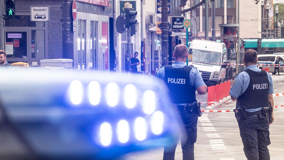 Polizeibeamte und ein Fahrzeug mit Blaulicht stehen vor einer Filiale der Frankfurter Sparkasse an der Düsseldorfer Straße. Auf die Filiale wurde ein Raubüberfall verübt.