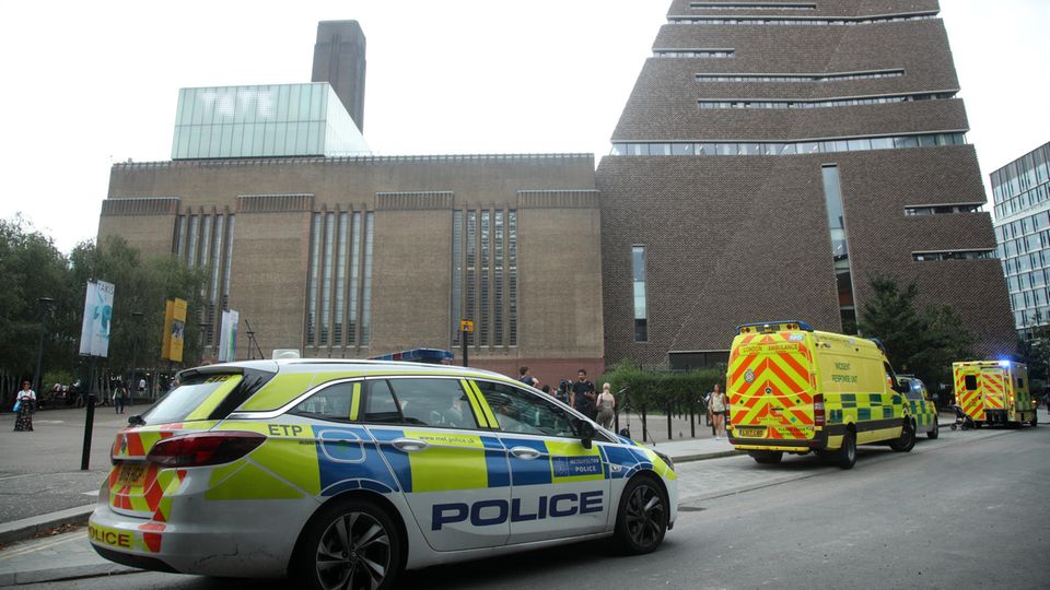 Vor einem hohen Backsteingebäude in London stehen zwei Polizeiwagen und ein Krankenwagen mit Blaulicht