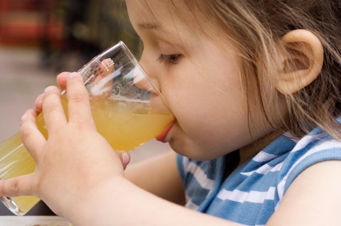 Ein dunkelblondes kleines Mädchen führt mit beiden Händen ein Glas Apfelsaft zum Mund