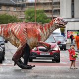 Die dreijährige Freya Smith hilft einem Dino über die Straße. Die Urtier-Figur gehört zur Performance der australischen Theatergruppe Erth, die mit ihrer Show "Dinosaurier-Zoo" am Fringe-Festival teilnimmt. Das Fringe findet jedes Jahr über mehrere Wochen im August im schottischen Edinburgh statt und ist mit seinen Tausenden Theaterstücken, Performances und Straßenkunst-Darbietungen das größte Kulturfestival der Welt.