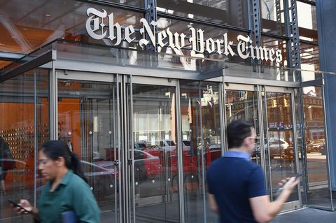 Vor einem gläsernen Eingang unter einem "The New York Times" Schriftzug laufen Menschen mit Smartphone in der Hand vorbei